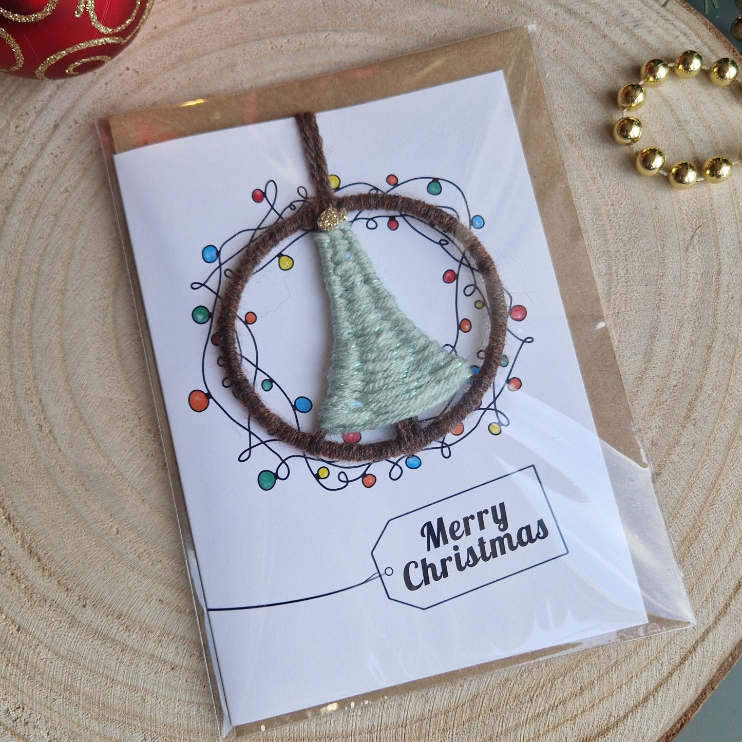 Card with a small woven duck egg blue tree on a wooden surface with Christmas decorations.