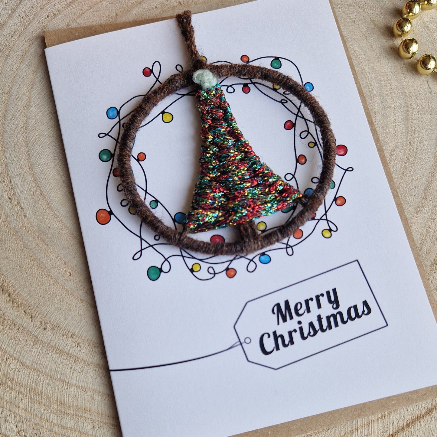 Handmade Christmas card with a fairy light design with a handwoven Christmas tree ornament on a wooden surface