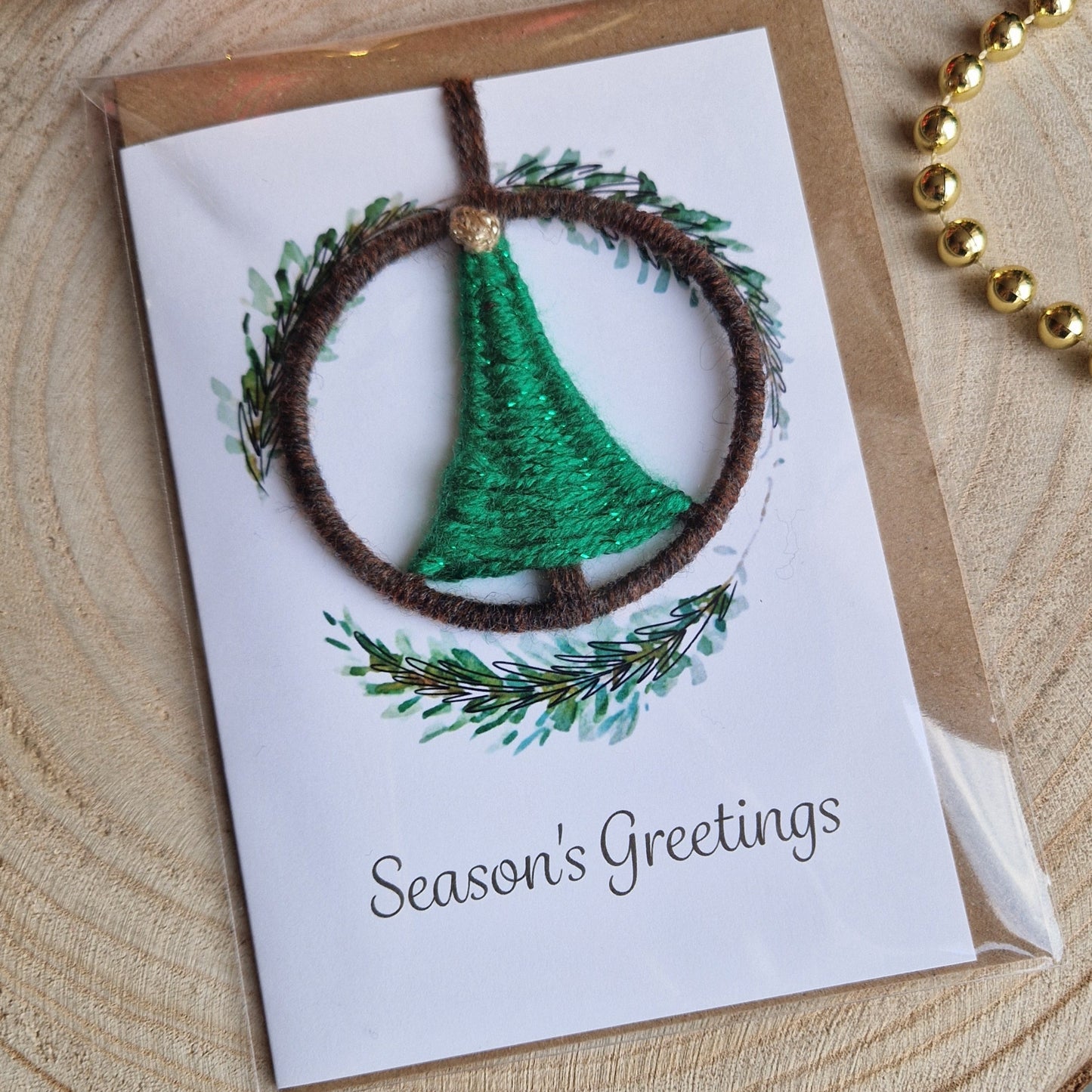 Christmas card with green pine wreath design on a wooden surface with ornaments.