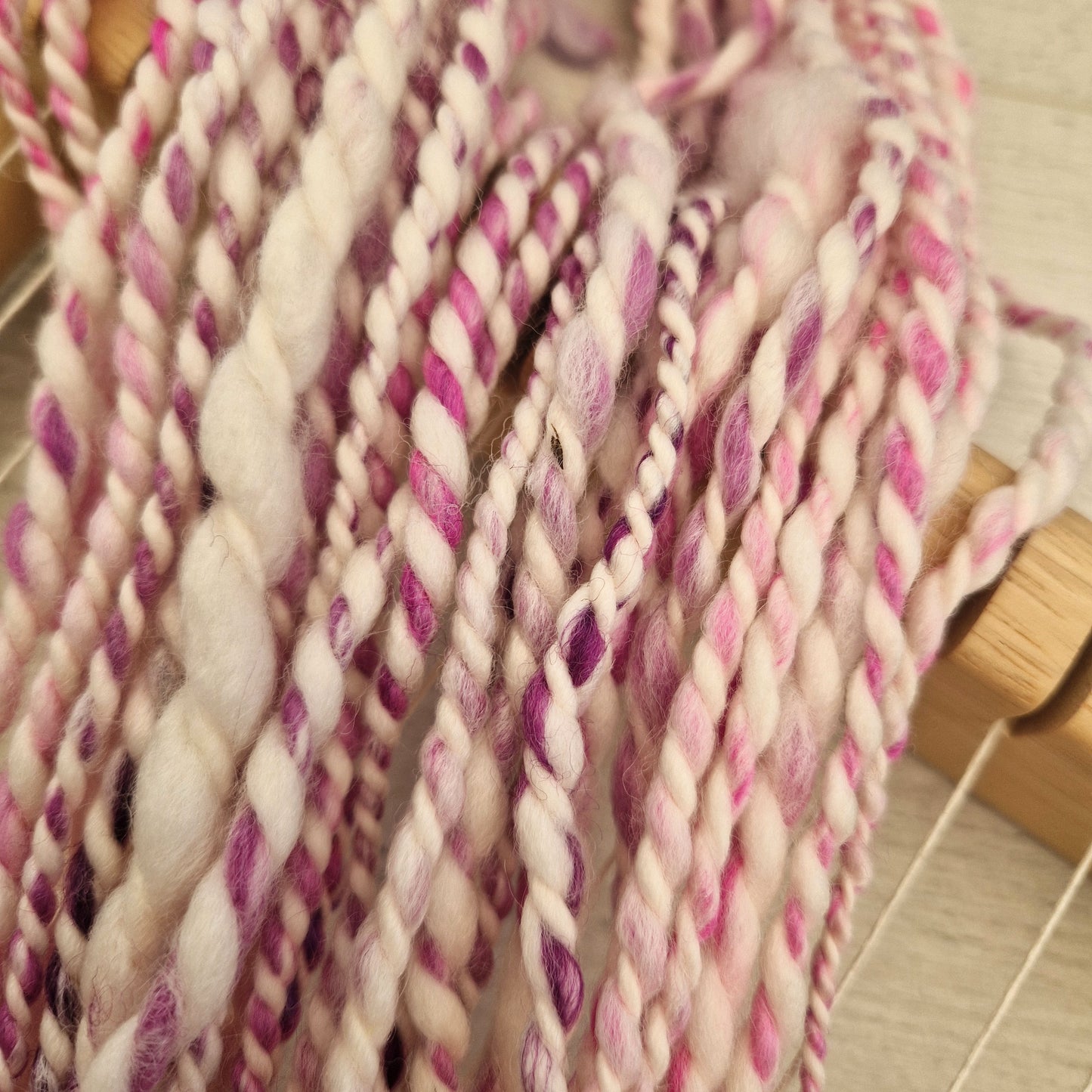 Close-up of pink and white yarn strands on a wooden surface