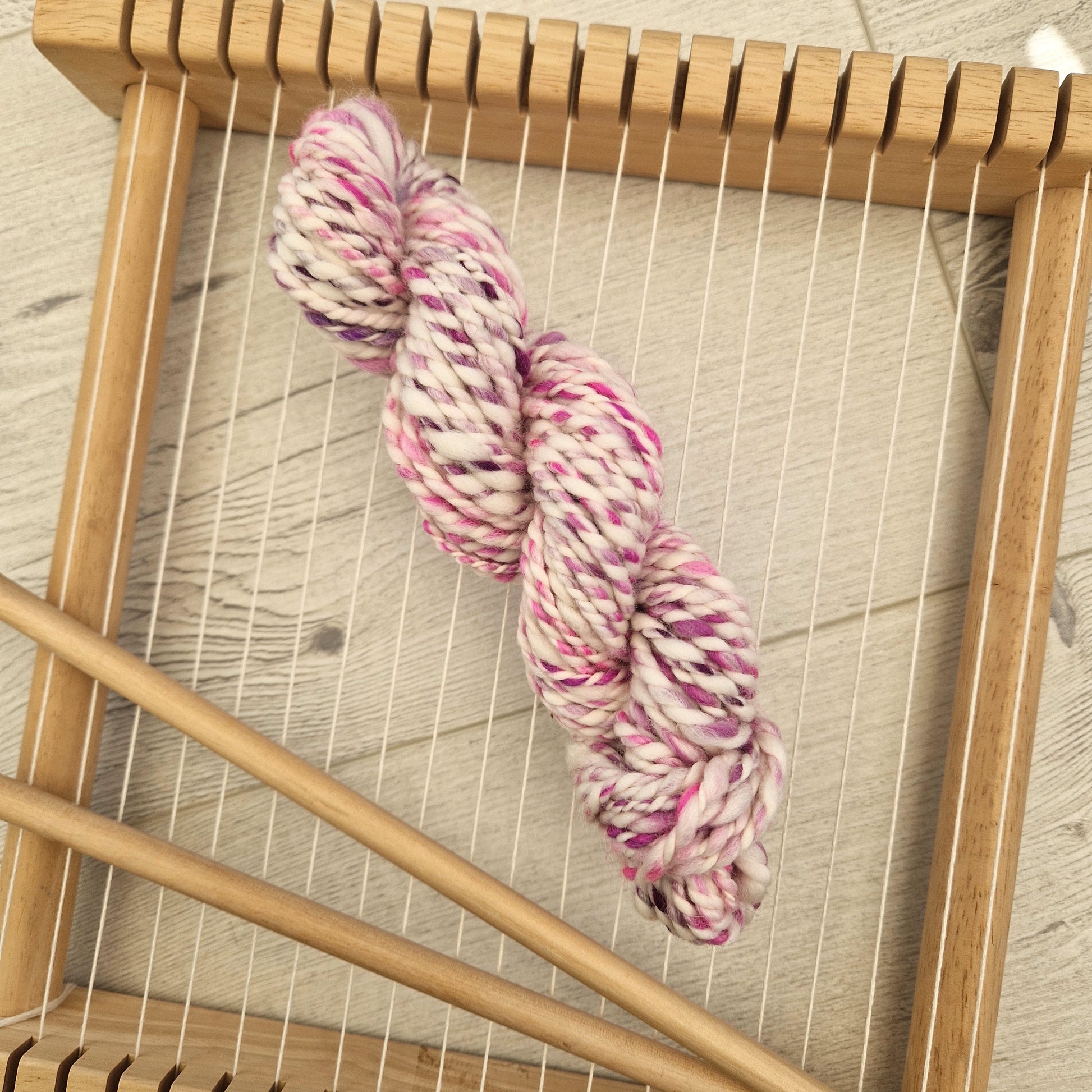 Spool of pink and white yarn on a wooden loom