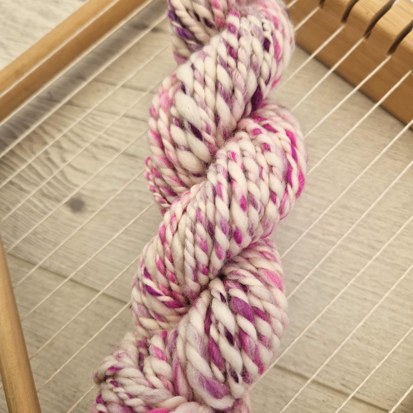 Skein of pink and white yarn on a wooden loom