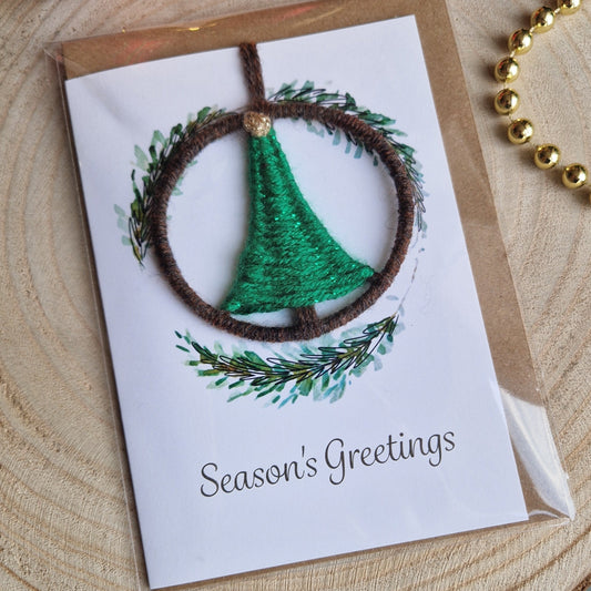 Christmas card with green pine wreath design on a wooden surface with ornaments.