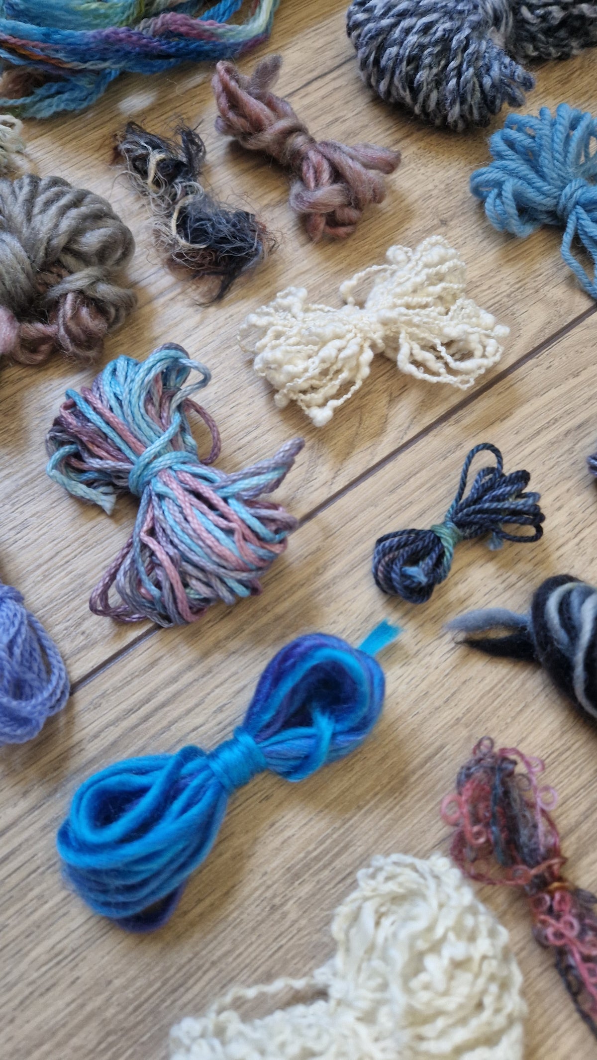 An assortment of colorful variegated yarn skeins and bundles arranged on a light wooden surface.