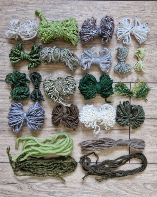 A flat-lay arrangement of various skeins and bundles of yarn in different colors and textures, organized in rows on a light brown wooden floor.