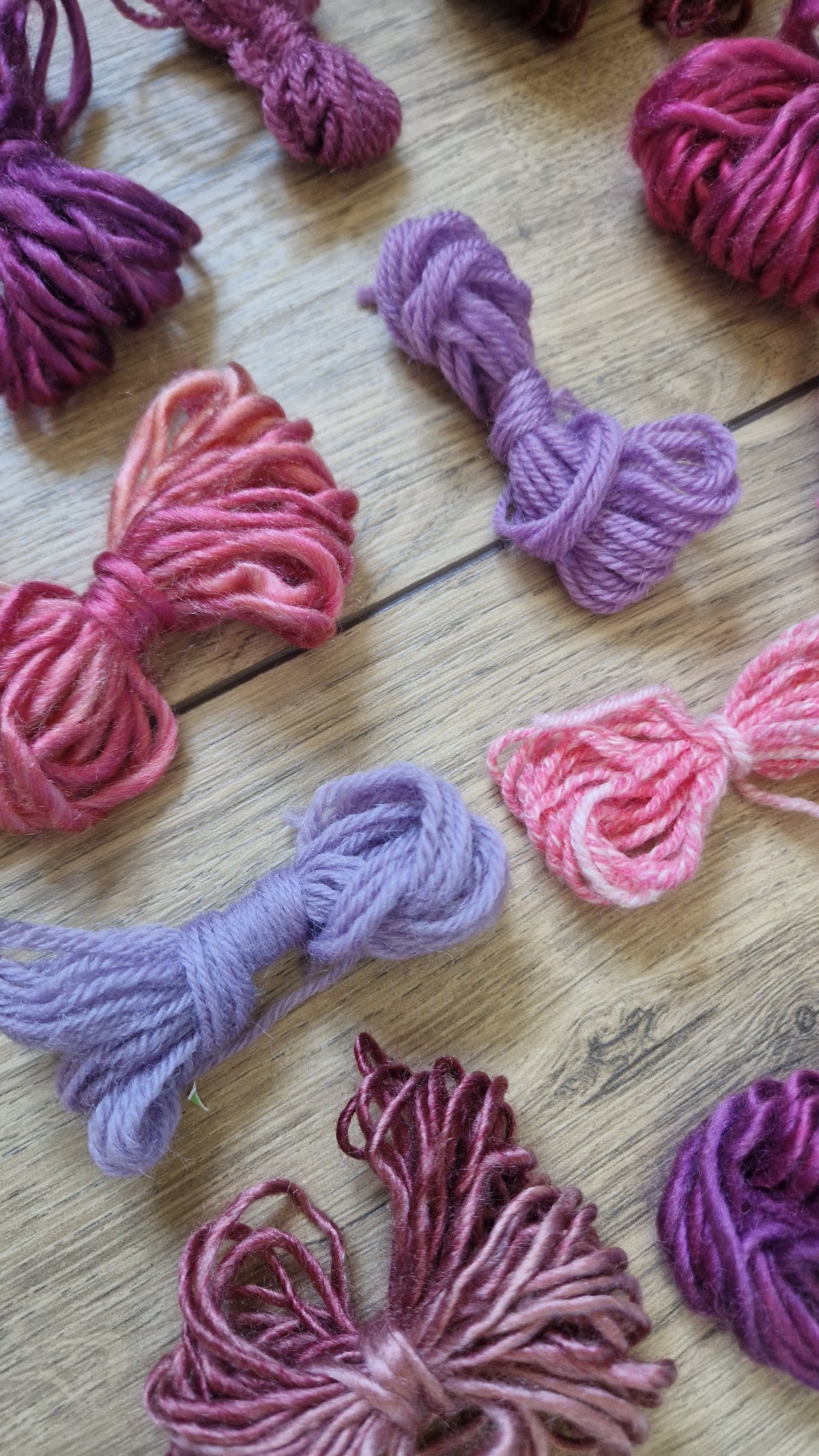 Multiple skeins of variegated yarn in shades of purple, pink, and burgundy arranged on a light wood surface.