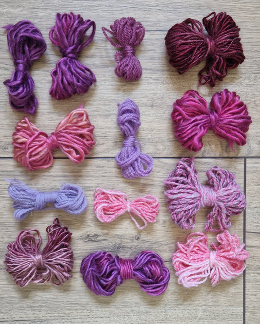 Skeins of variegated yarn in shades of purple, pink, and magenta, arranged in a grid on a light brown wood plank background.