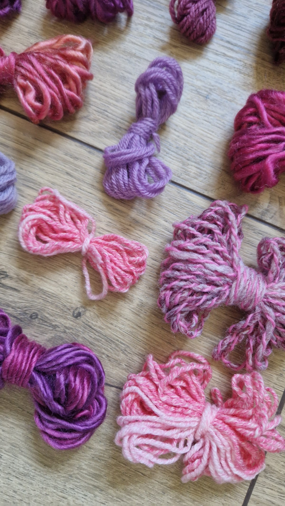 Multiple skeins of variegated yarn in shades of pink, purple, and magenta arranged on a light wood surface.